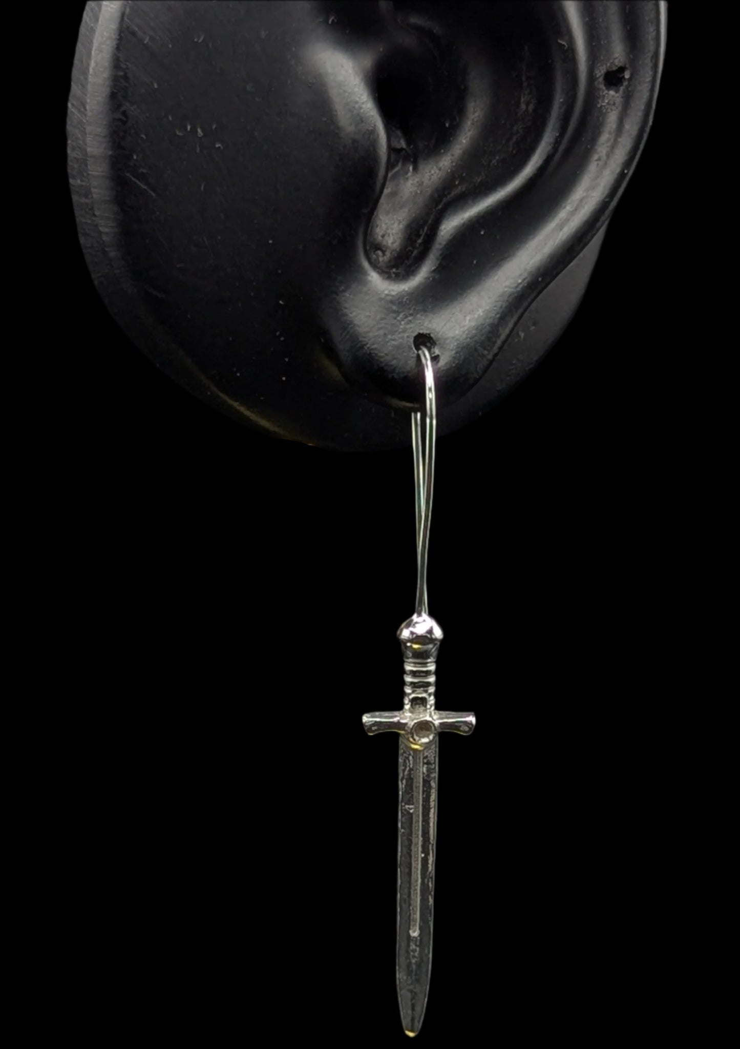 Silver dagger-shaped earring on a black background
