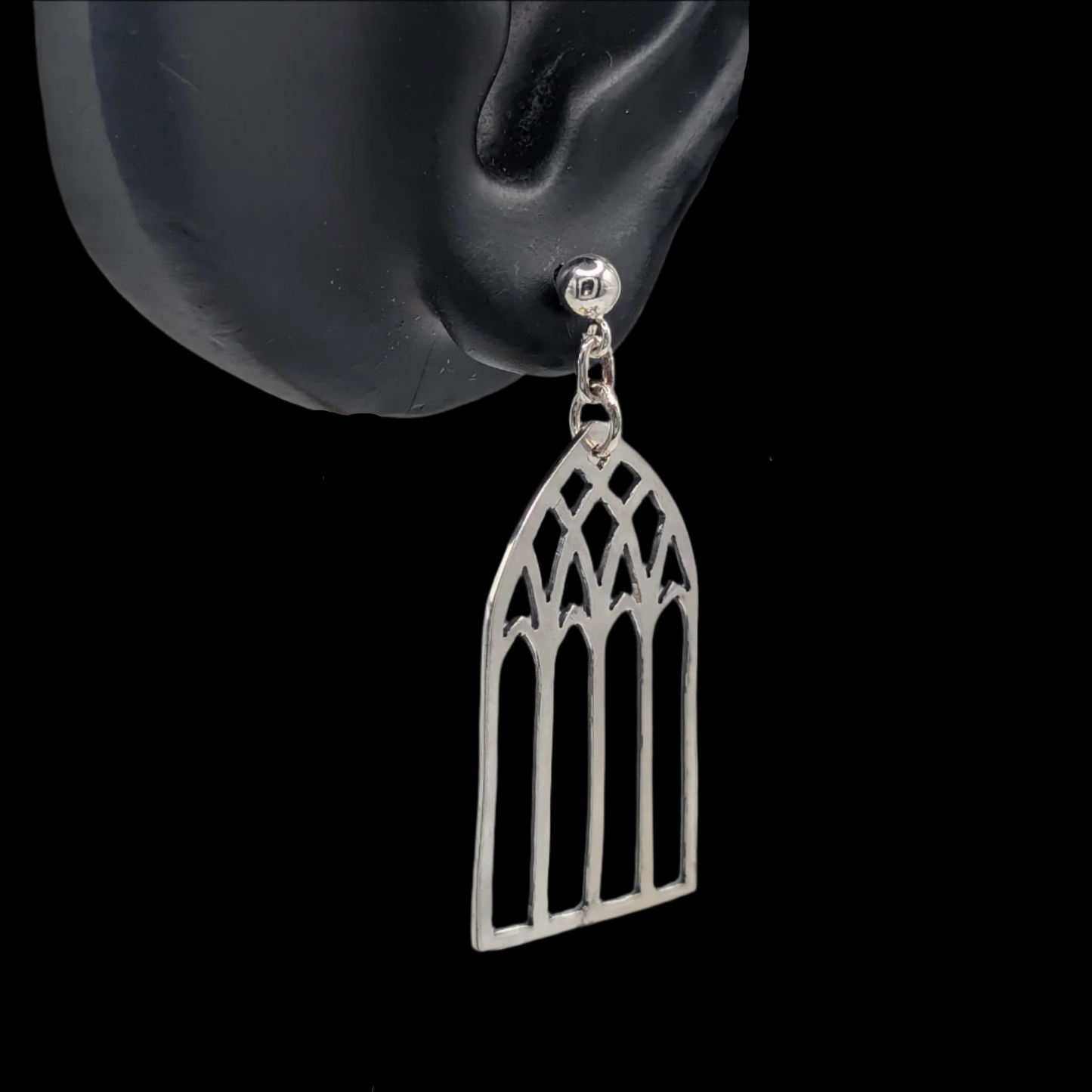 A pair of silver stud earrings designed to resemble cathedral windows, displayed on a mannequin ear.