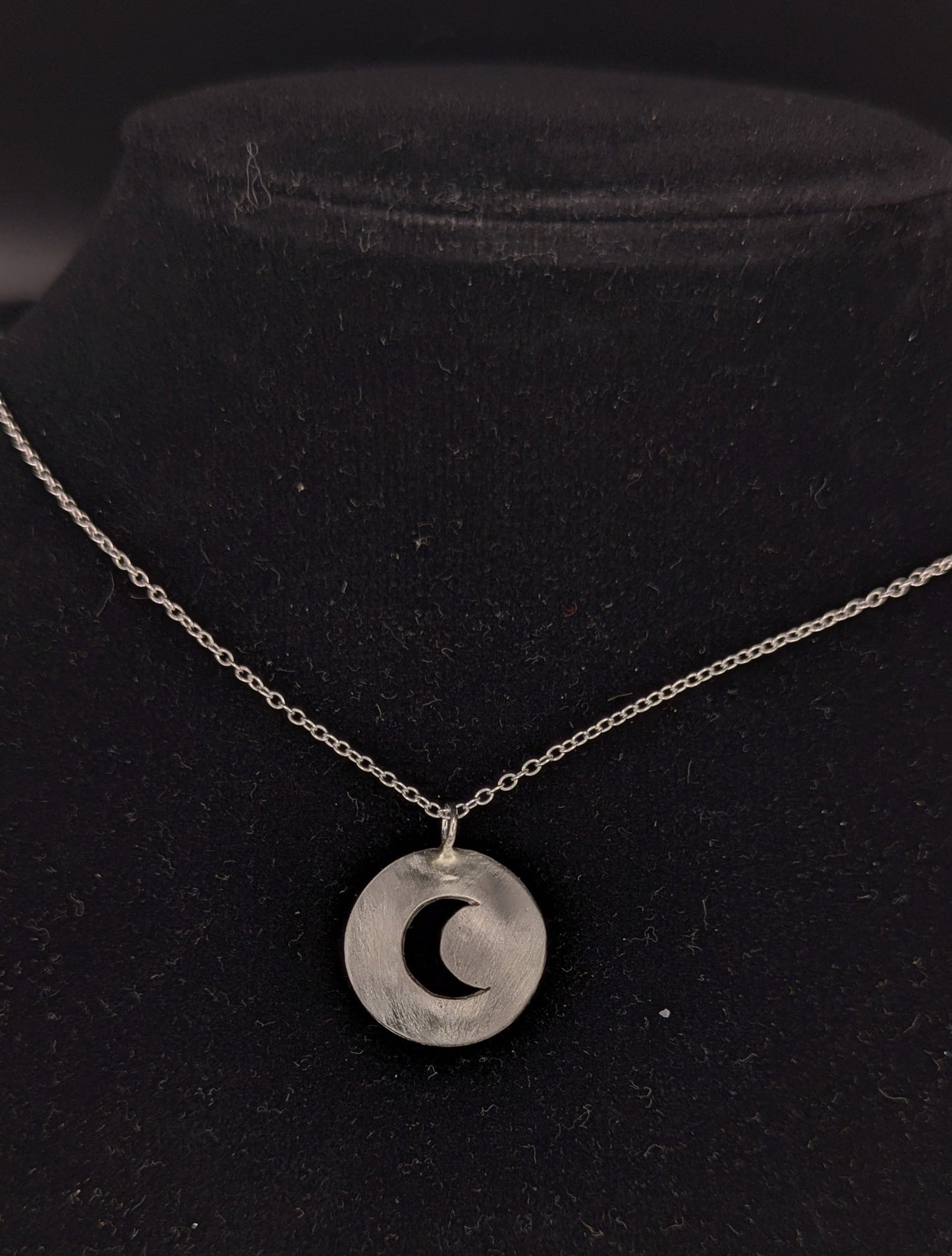 Silver necklace with a crescent moon pendant on a black background
