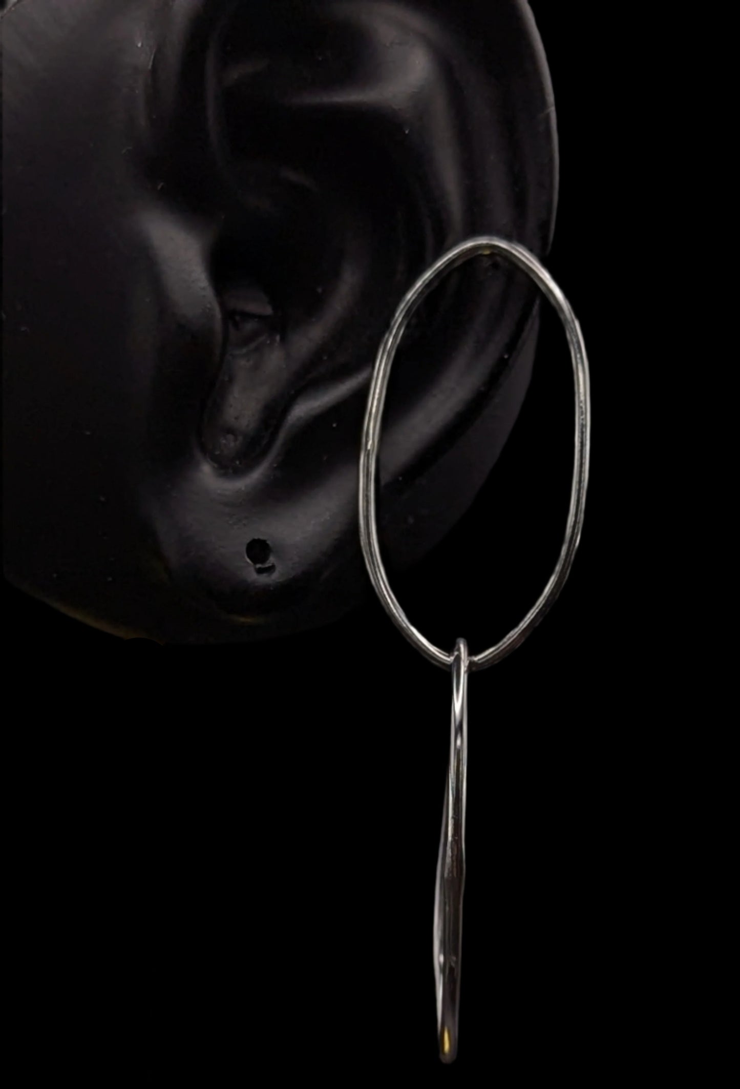 Silver hoop earring with a dangling element on a black background