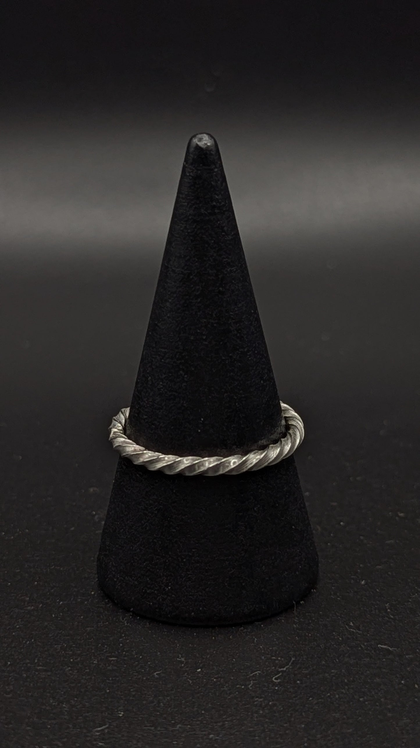 Black cone-shaped object with a silver ring on a dark background