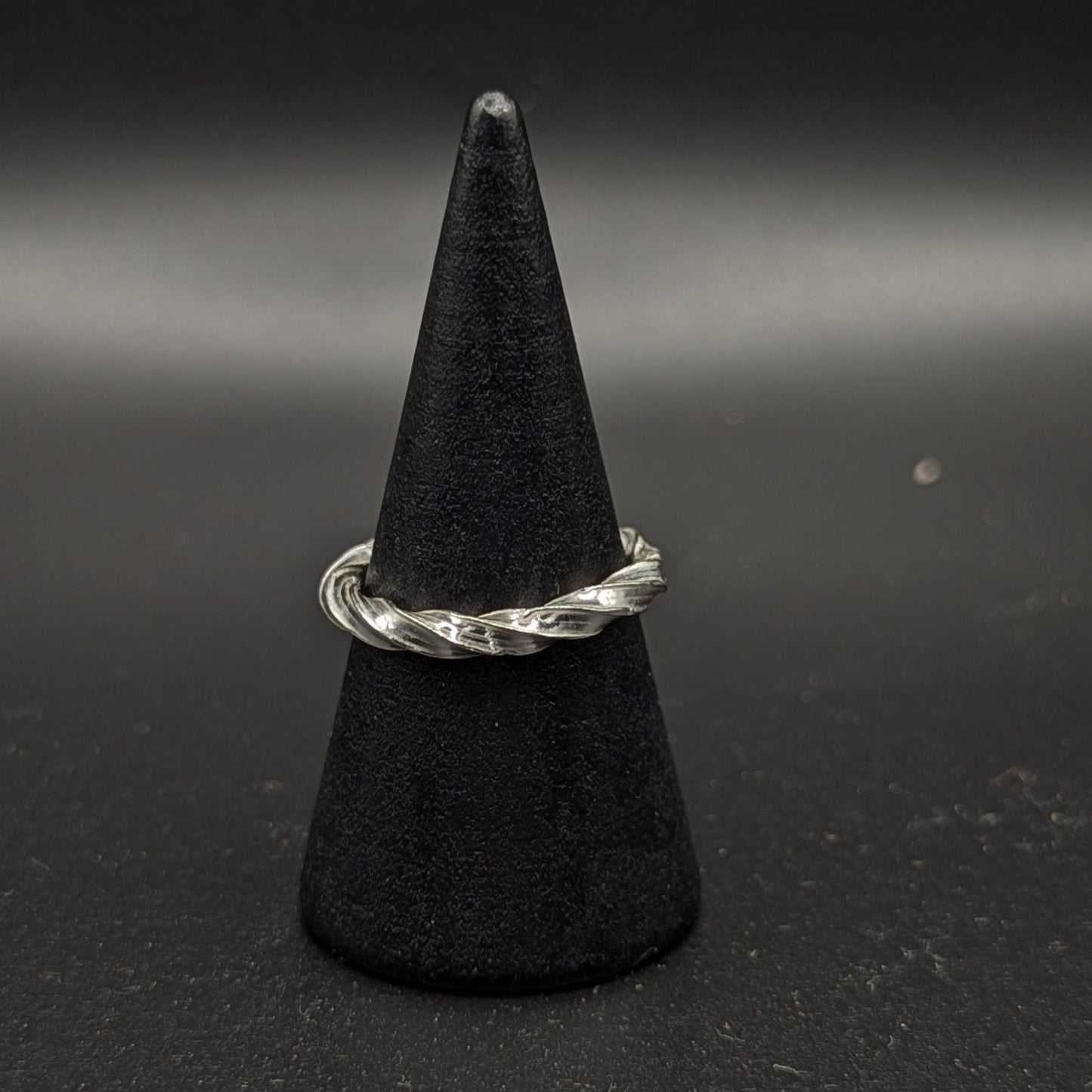 Silver ring on a black cone-shaped stand against a dark background