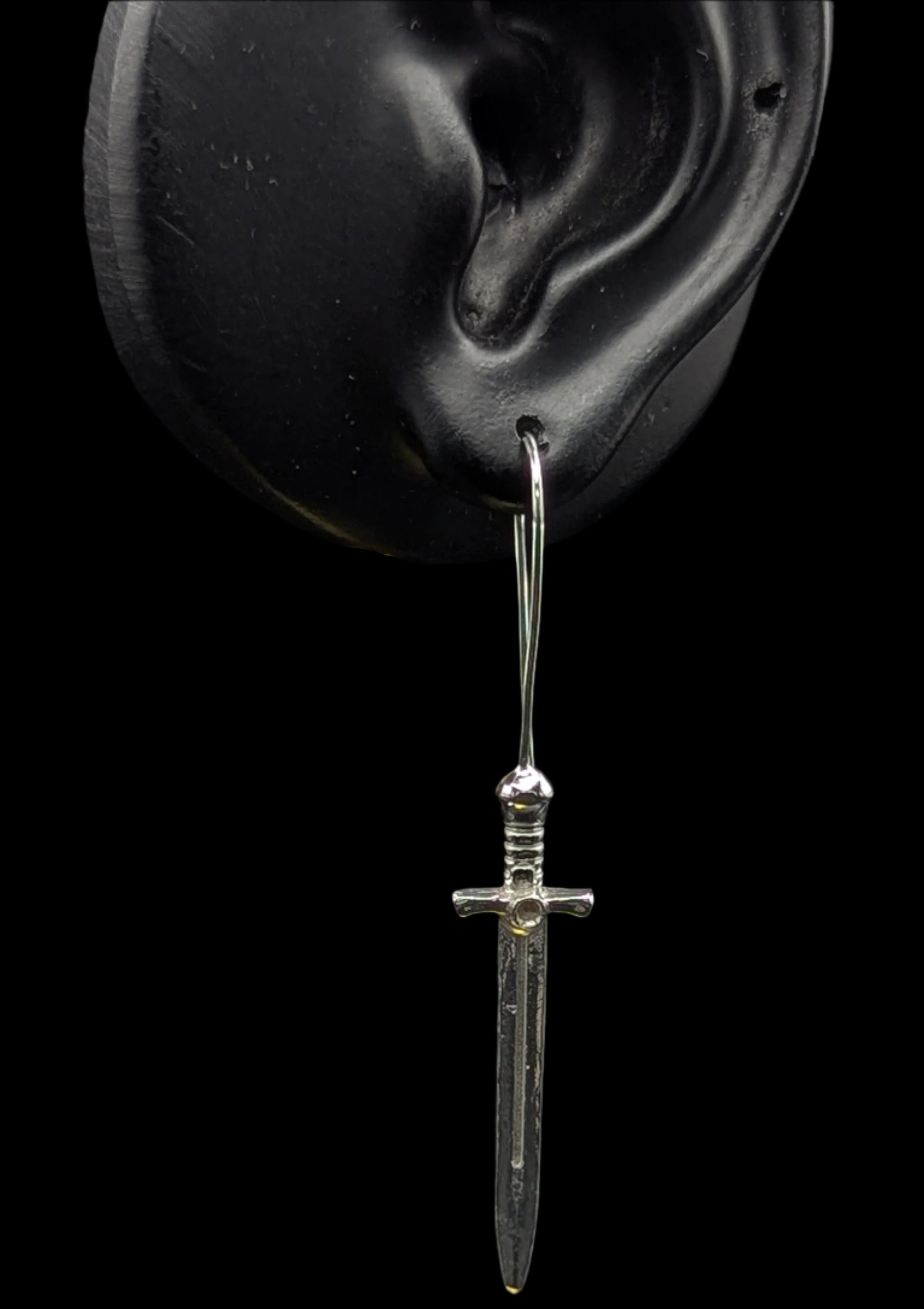 Silver dagger-shaped earring on a black background