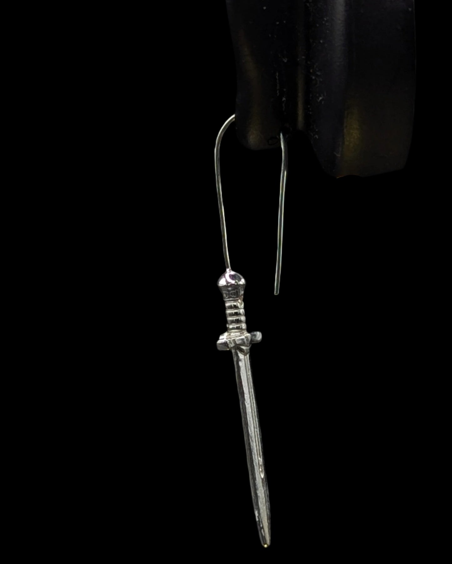 Silver dagger-shaped earring on a black background