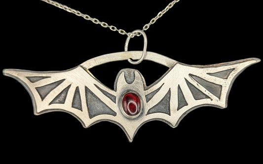 Silver bat-wing shaped pendant with a red gemstone on a dark background