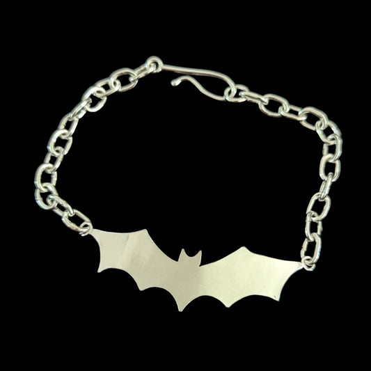 Bat-shaped bracelet on a black surface with black background