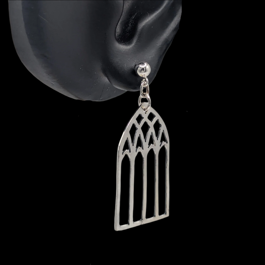 A pair of silver stud earrings designed to resemble cathedral windows, displayed on a mannequin ear.