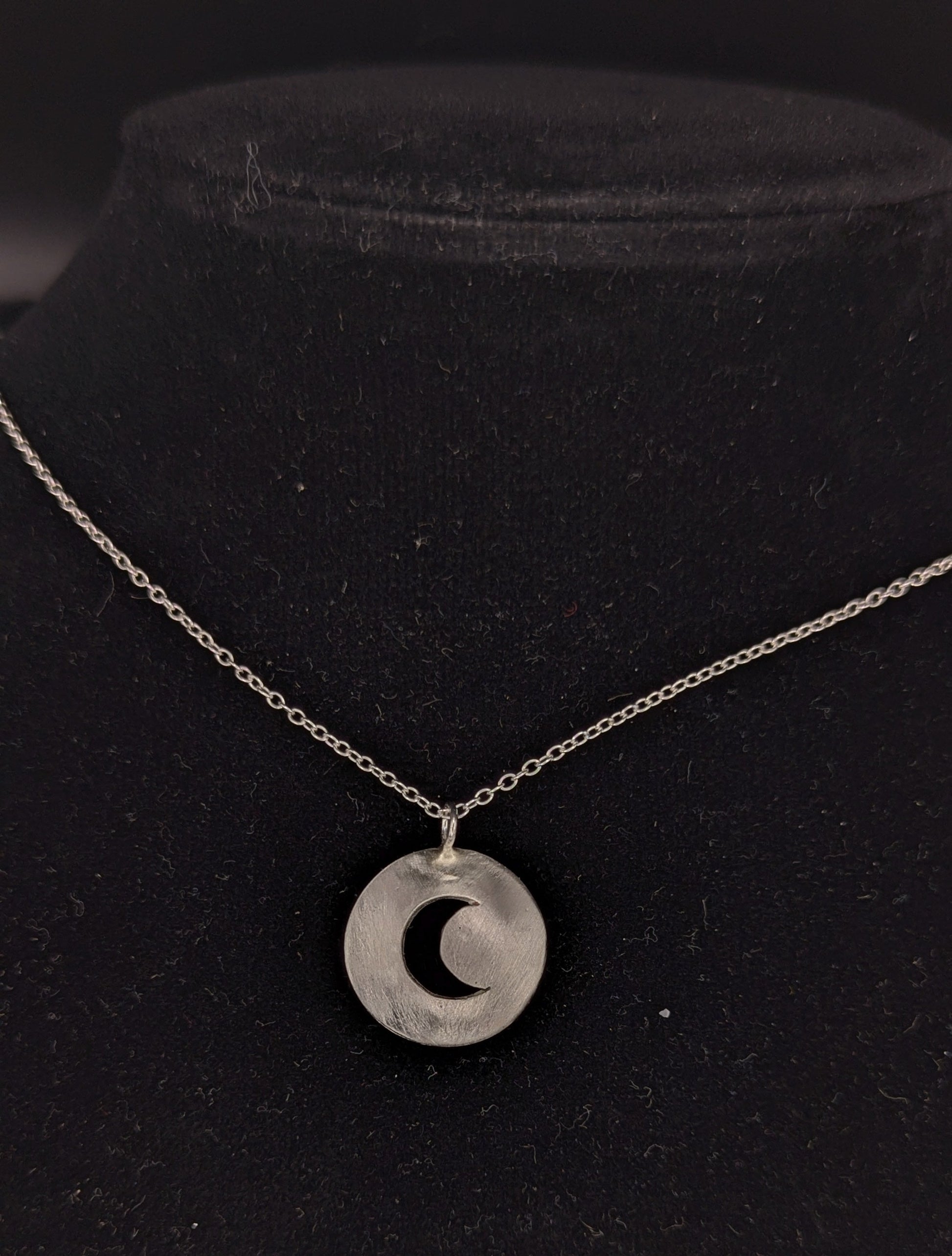 Silver necklace with a crescent moon pendant on a black background