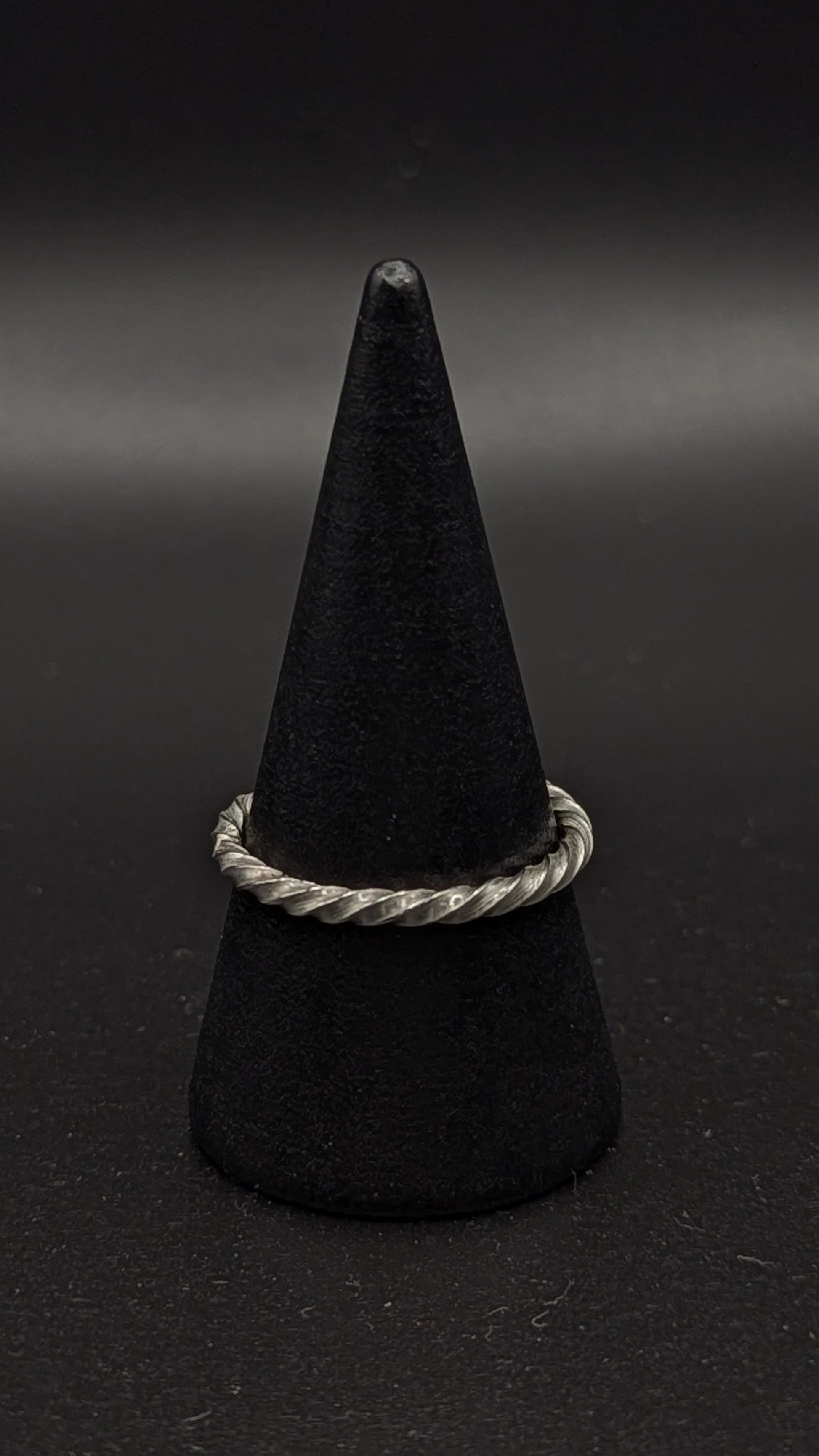 Black cone-shaped object with a silver ring on a dark background