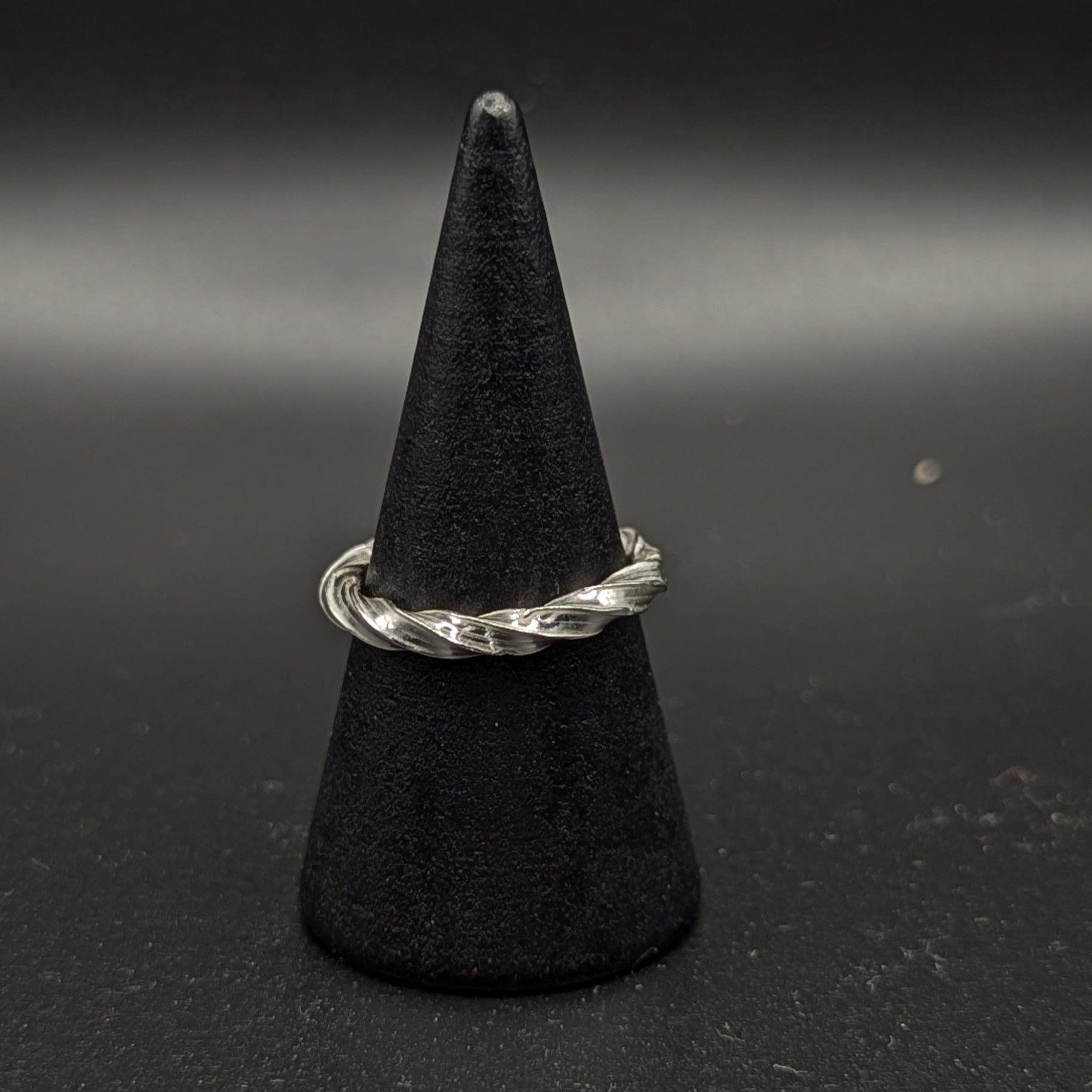 Silver ring on a black cone-shaped stand against a dark background