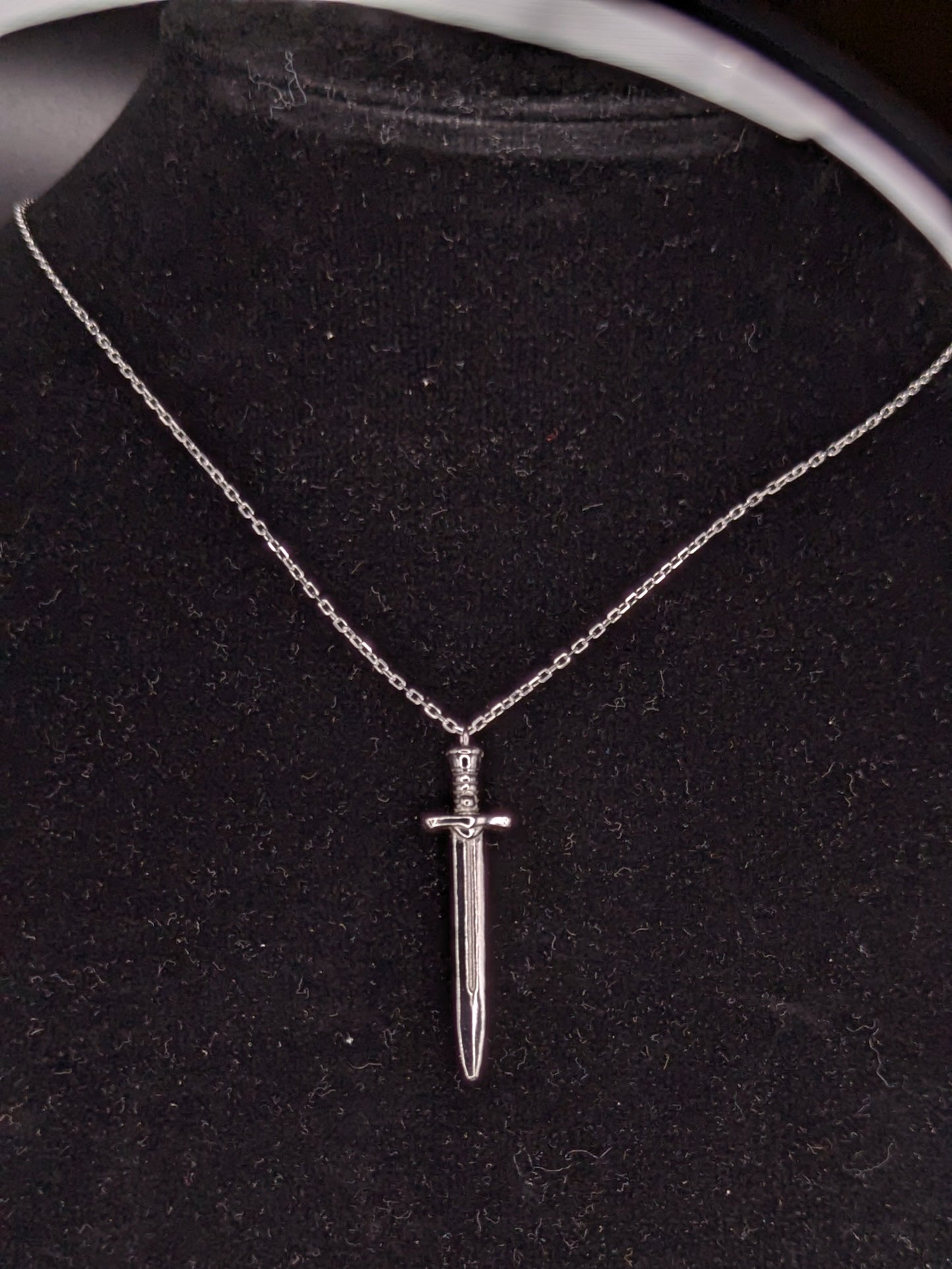 Silver dagger necklace on a black velvet stand